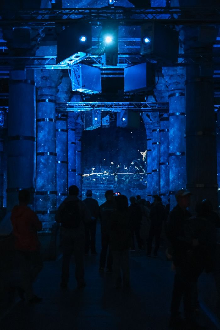 our-story Blue-themed illumination in a dark indoor venue with silhouetted audience watching an engaging performance.