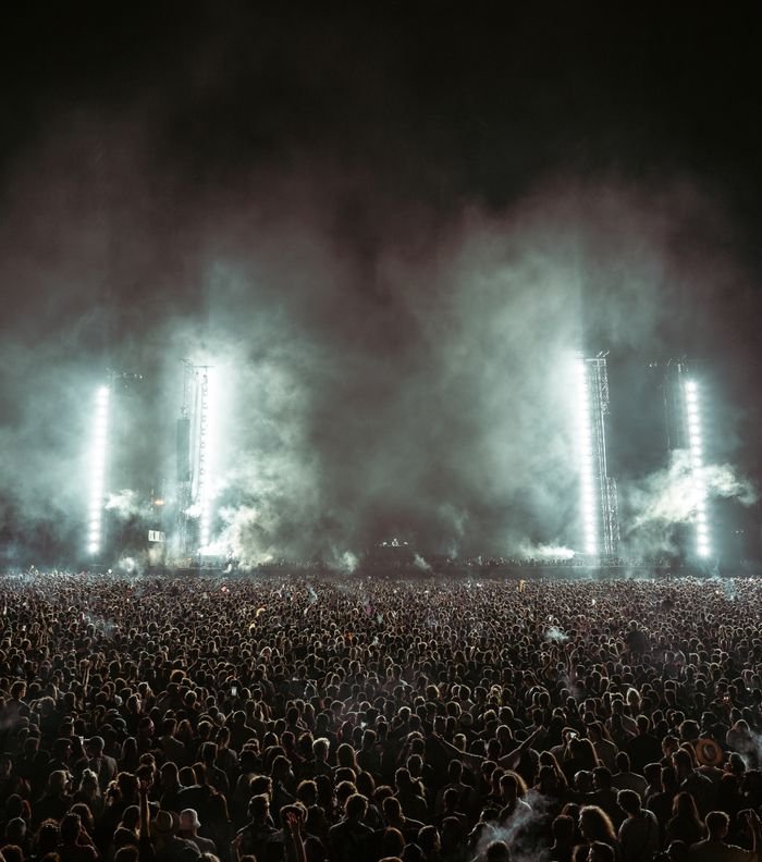Captivating shot of a massive crowd enjoying a music festival under bright stage lights at night.