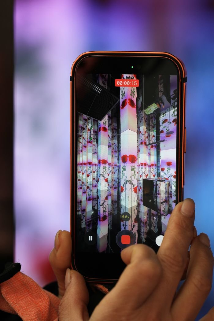 Crafting Captivating Headlines: Your awesome post title goes here A person recording a colorful digital art display on a smartphone indoors.